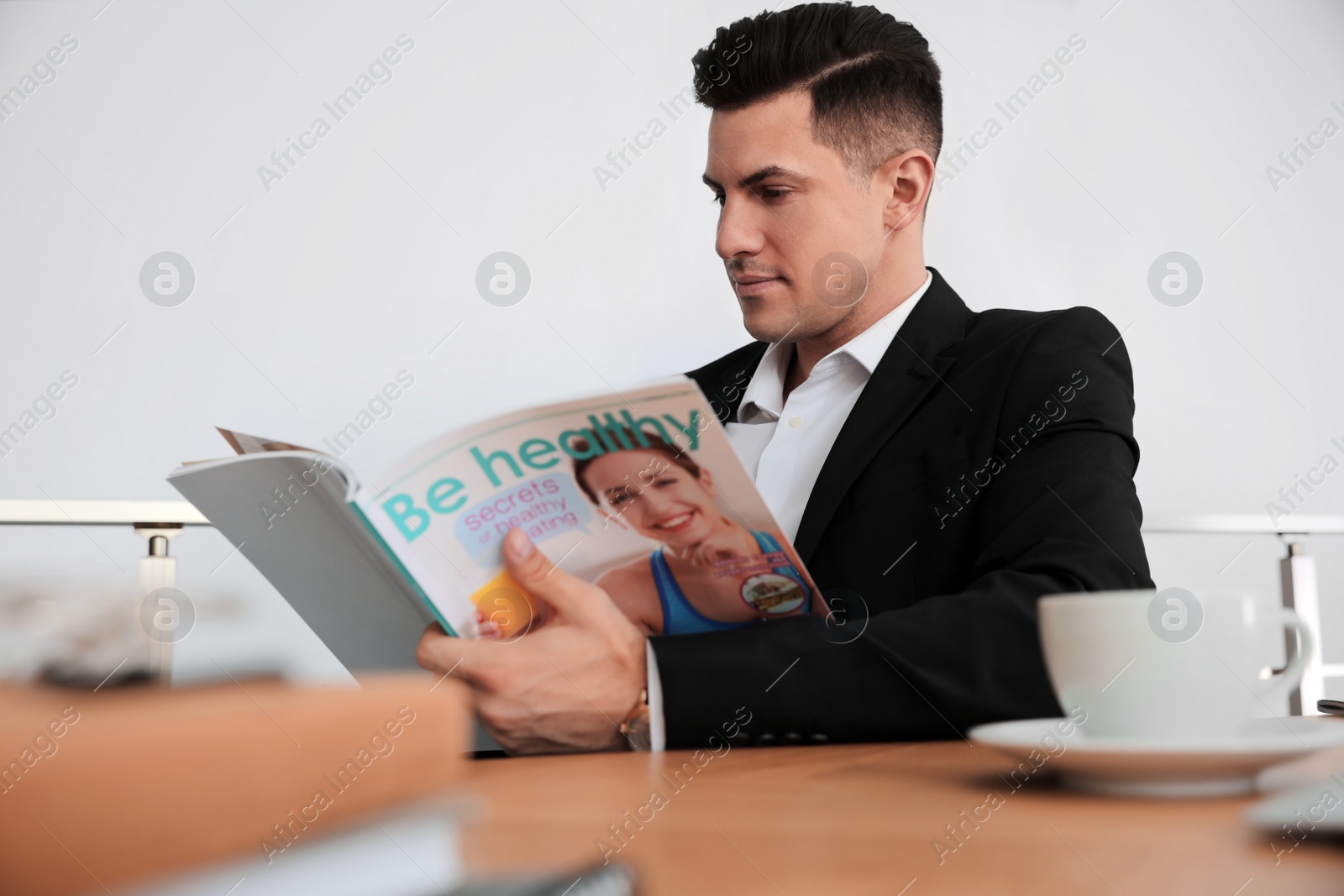 Photo of Man reading magazine at table in office