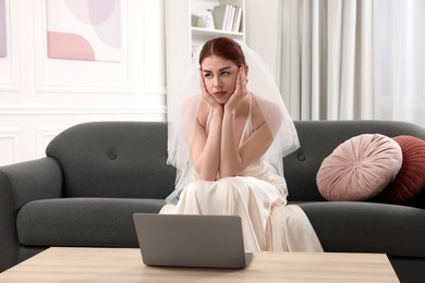 Unhappy bride with laptop on sofa in living room