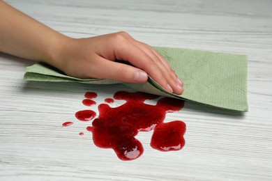 Photo of Woman wiping spilled jam with paper towel on wooden table, closeup