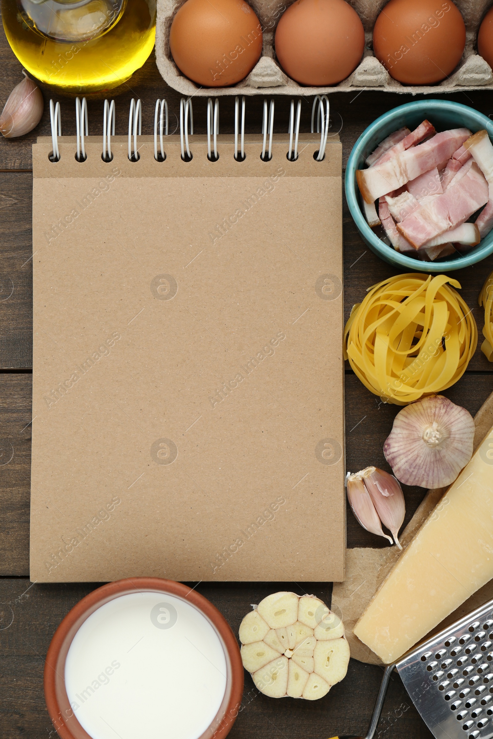 Photo of Blank recipe book and different ingredients on wooden table, flat lay. Space for text