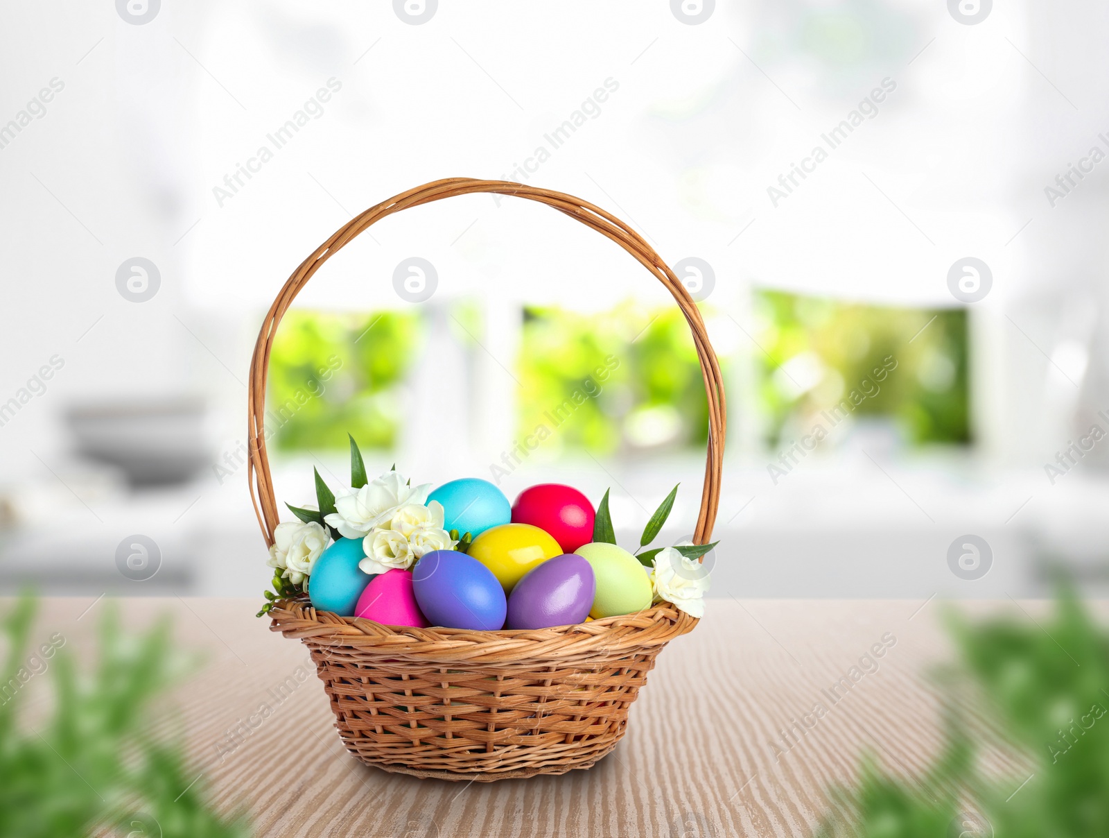 Image of Wicker basket with bright painted Easter eggs and spring flowers on wooden table