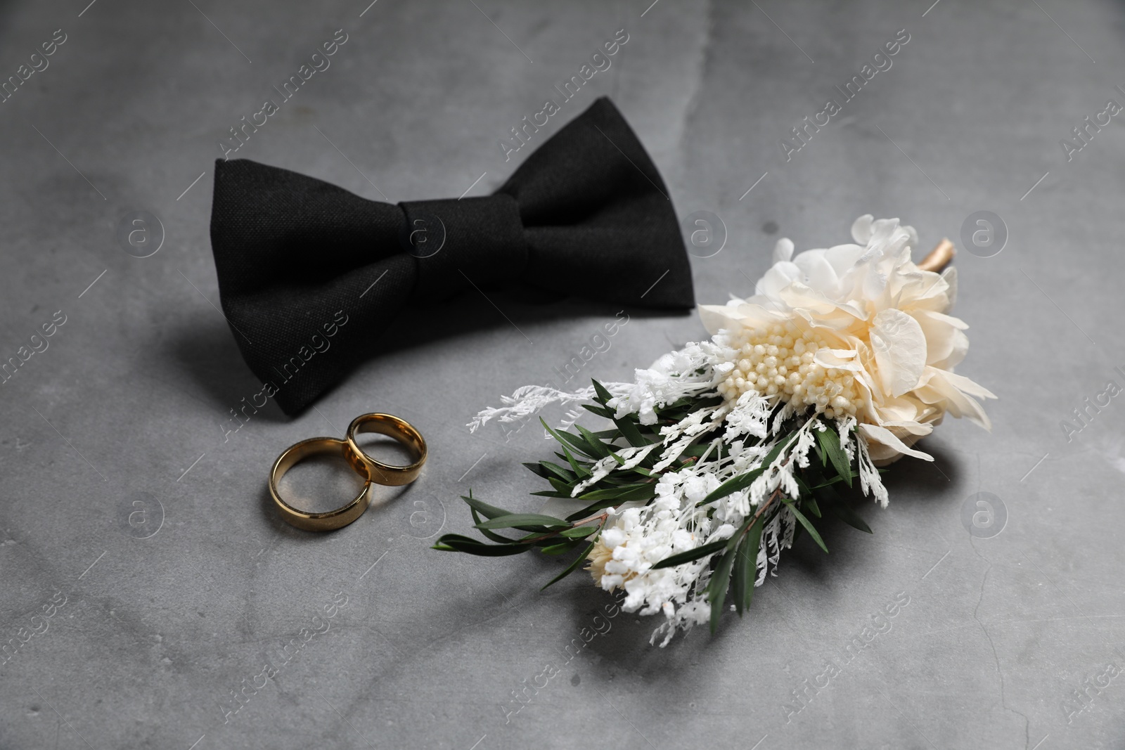 Photo of Wedding stuff. Stylish boutonniere, bow tie and wedding rings on gray background