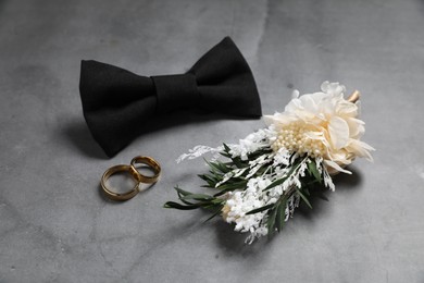 Wedding stuff. Stylish boutonniere, bow tie and wedding rings on gray background
