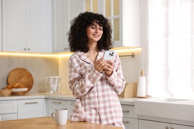 Photo of Beautiful young woman in stylish pyjama with smartphone in kitchen