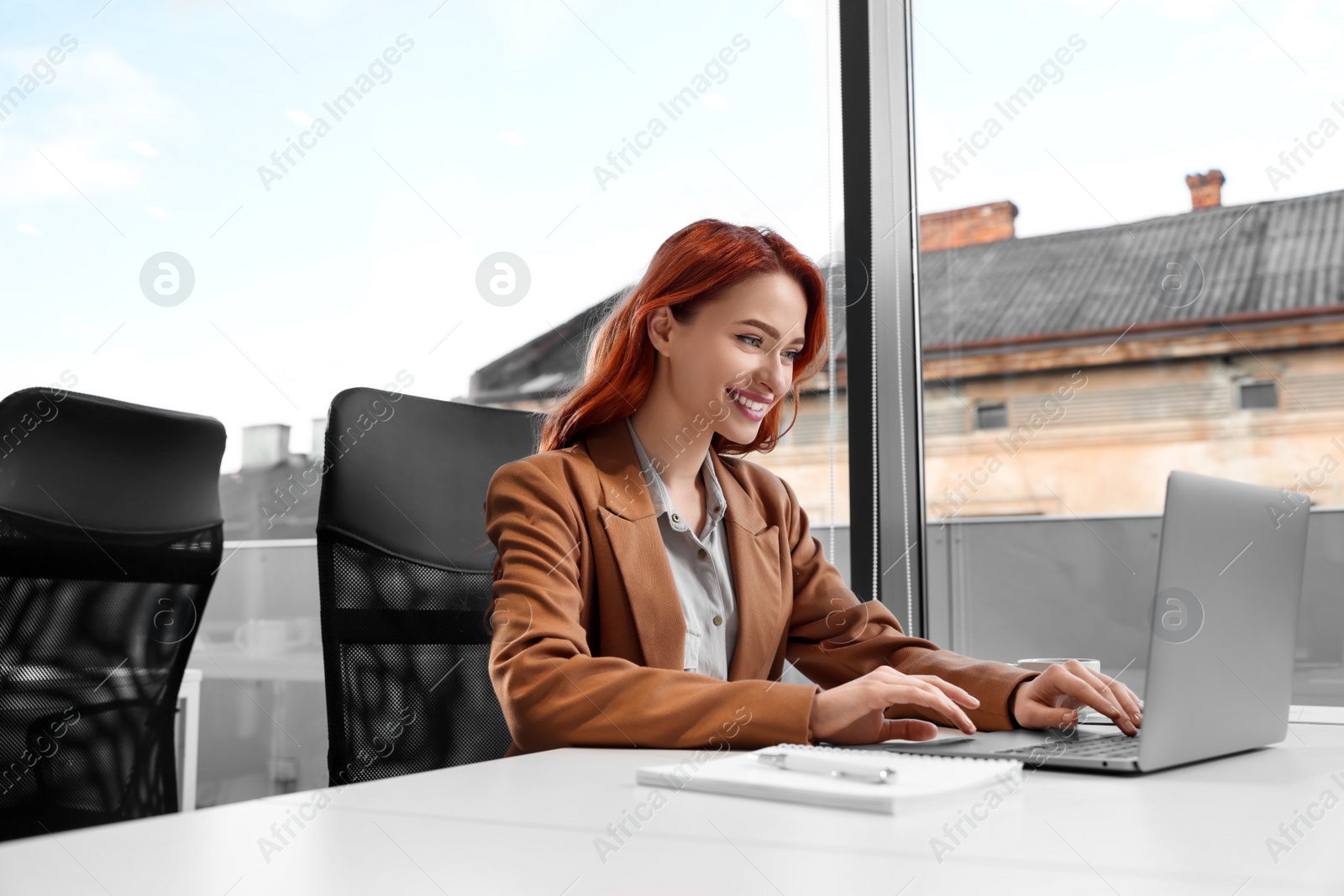 Photo of Happy woman working with laptop at white desk in office