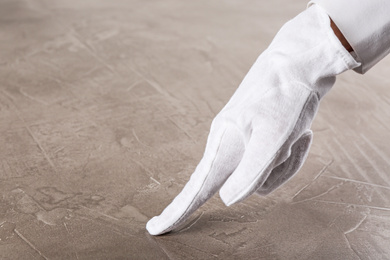 Photo of Person in white glove checking cleanliness of beige stone table, closeup