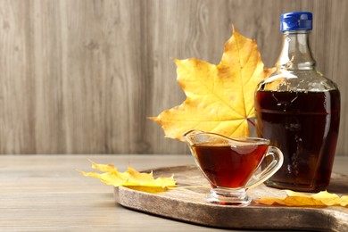 Bottle and gravy boat with tasty maple syrup on wooden table, space for text