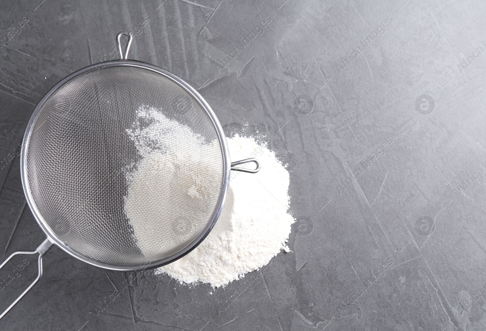 Photo of Metal sieve and flour on grey table, top view. Space for text