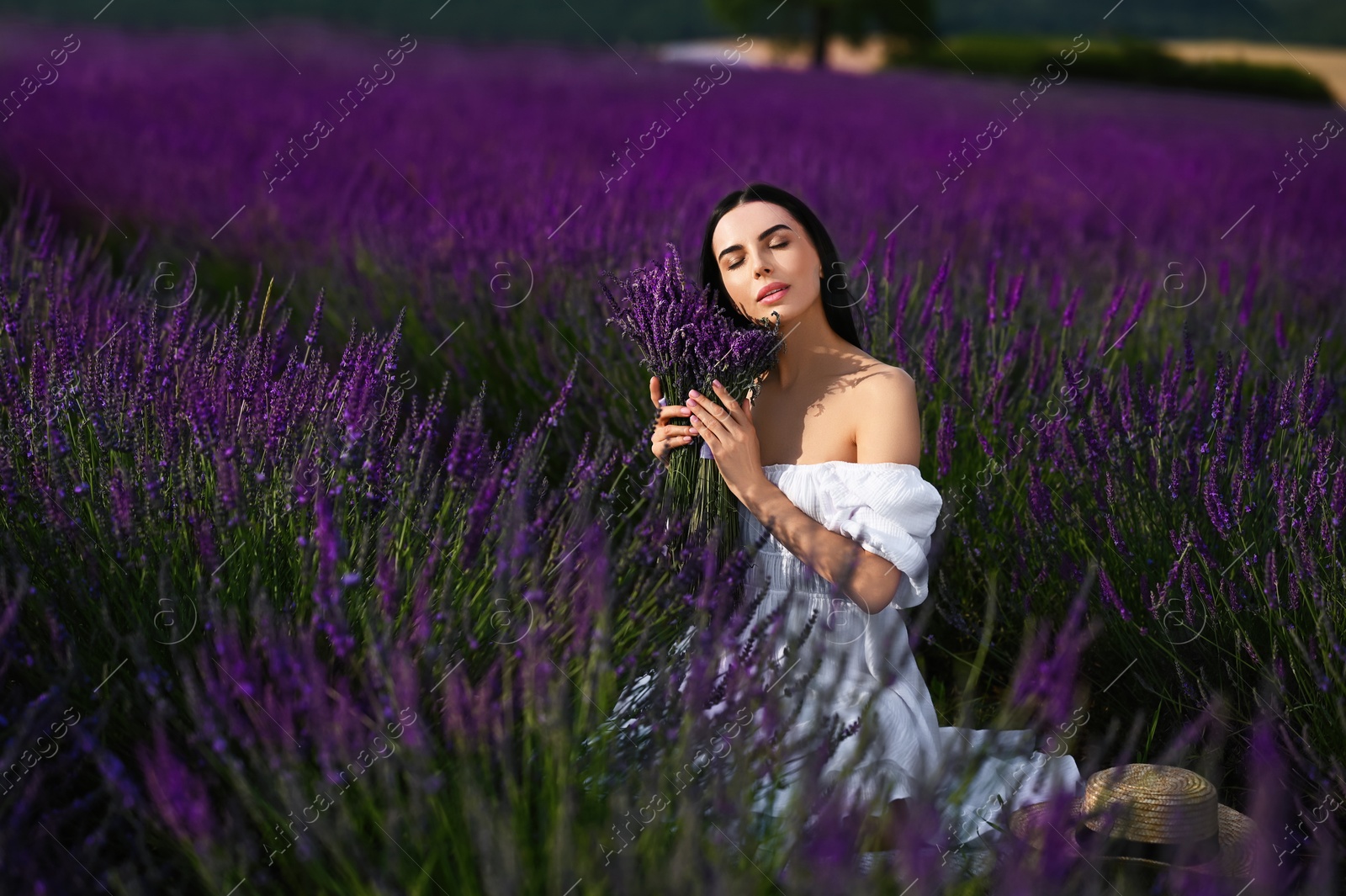 Photo of Beautiful young woman with bouquet sitting in lavender field