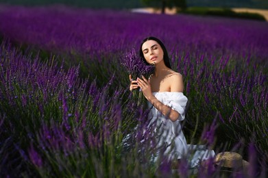 Beautiful young woman with bouquet sitting in lavender field