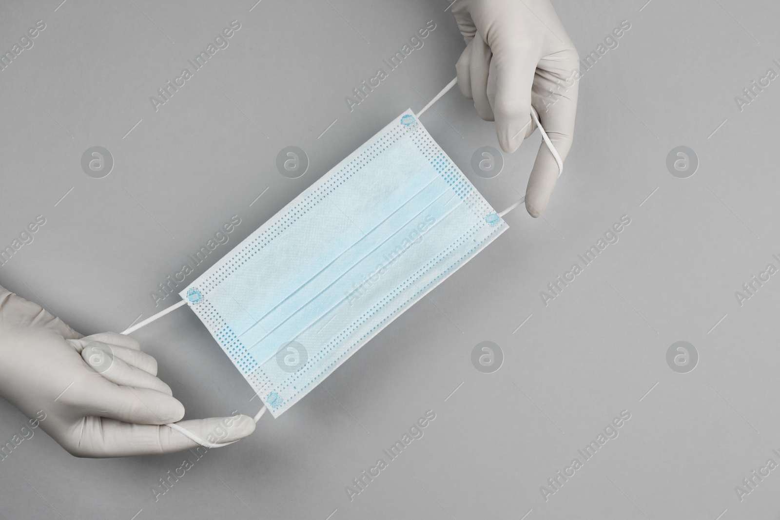 Photo of Doctor in medical gloves holding protective mask on light grey background, closeup. Space for text