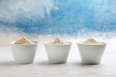 Photo of Bowls with different types of flour on table against color background. Space for text