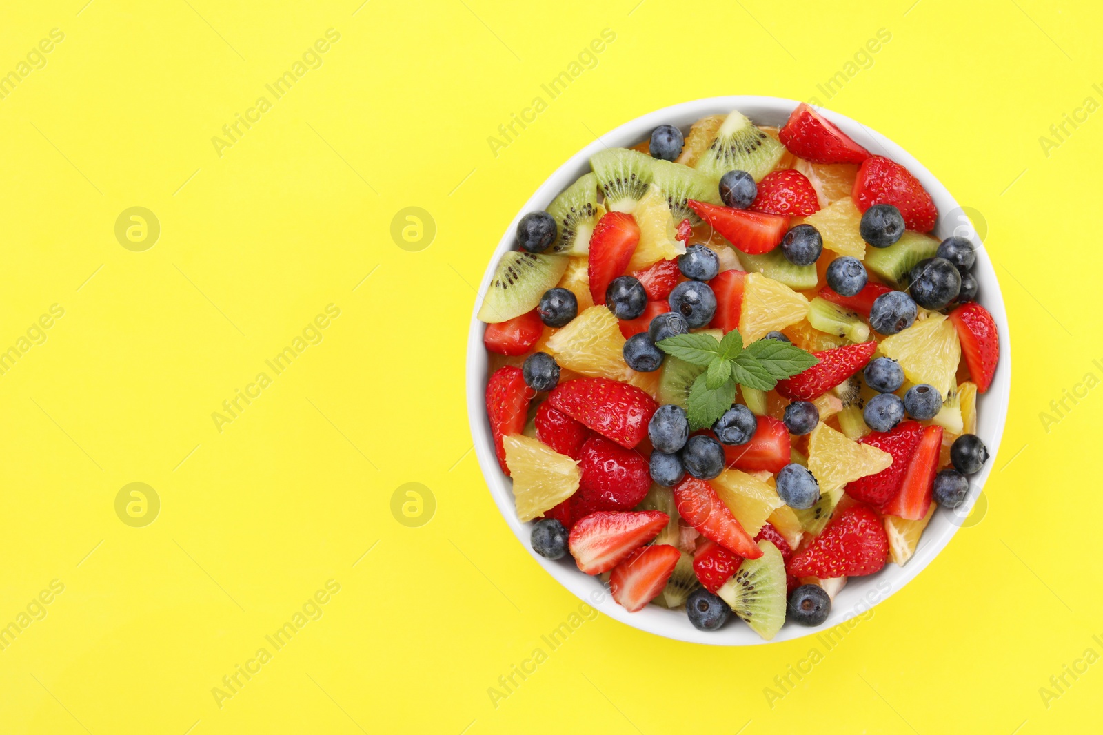 Photo of Yummy fruit salad in bowl on yellow background, top view. Space for text