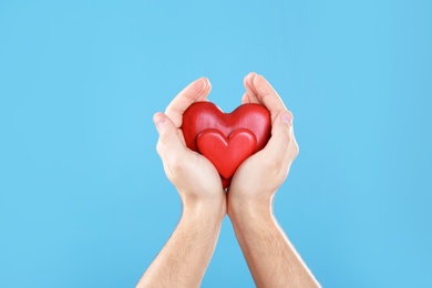 Photo of Man holding decorative hearts in hands on color background, closeup