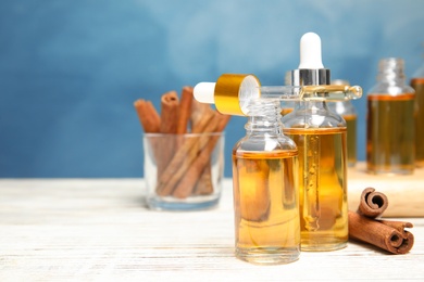 Photo of Bottles of essential oils and cinnamon sticks on table against blue background. Space for text