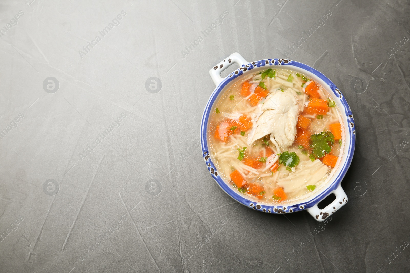 Photo of Homemade chicken soup in dish on grey background, top view with space for text