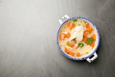 Homemade chicken soup in dish on grey background, top view with space for text