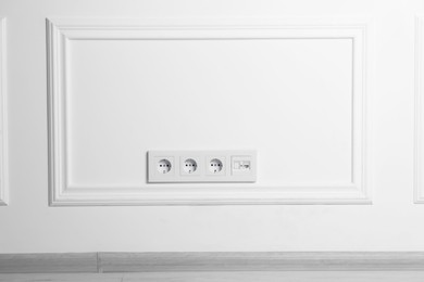 Electric power sockets on white wall, space for text