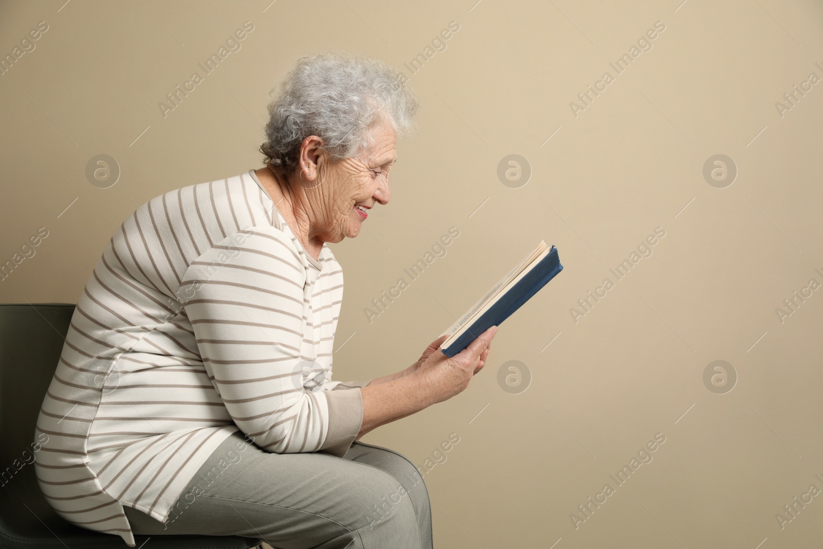 Photo of Elderly woman with poor posture reading book on beige background