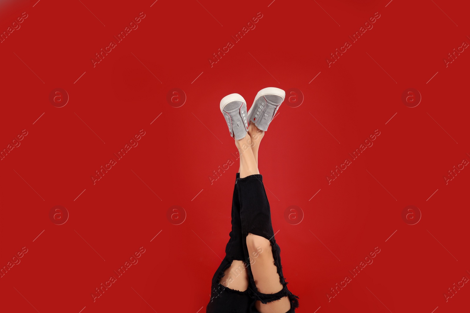 Photo of Woman in stylish sport shoes on red background