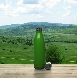 Wooden desk with thermos and mountain landscape on background