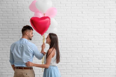 Photo of Young couple with air balloons near white brick wall. Celebration of Saint Valentine's Day