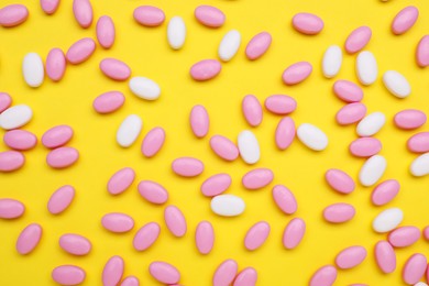Photo of Many colorful dragee candies on yellow background, flat lay