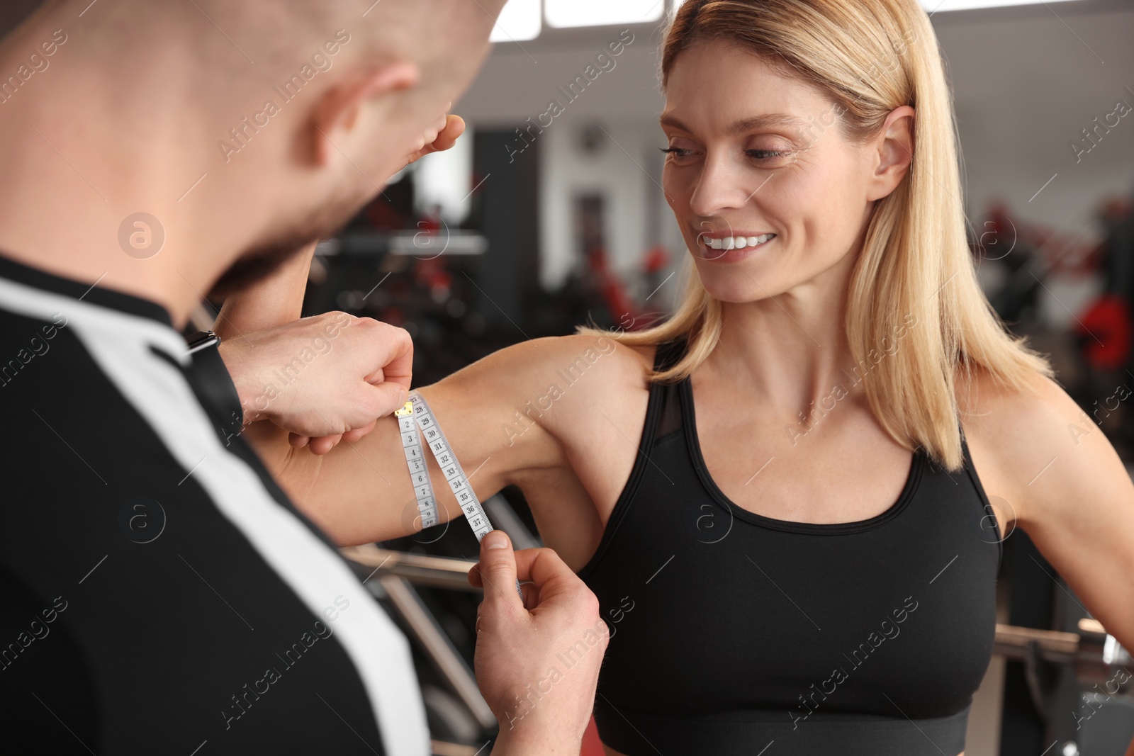 Photo of Trainer measuring woman`s biceps with tape in gym