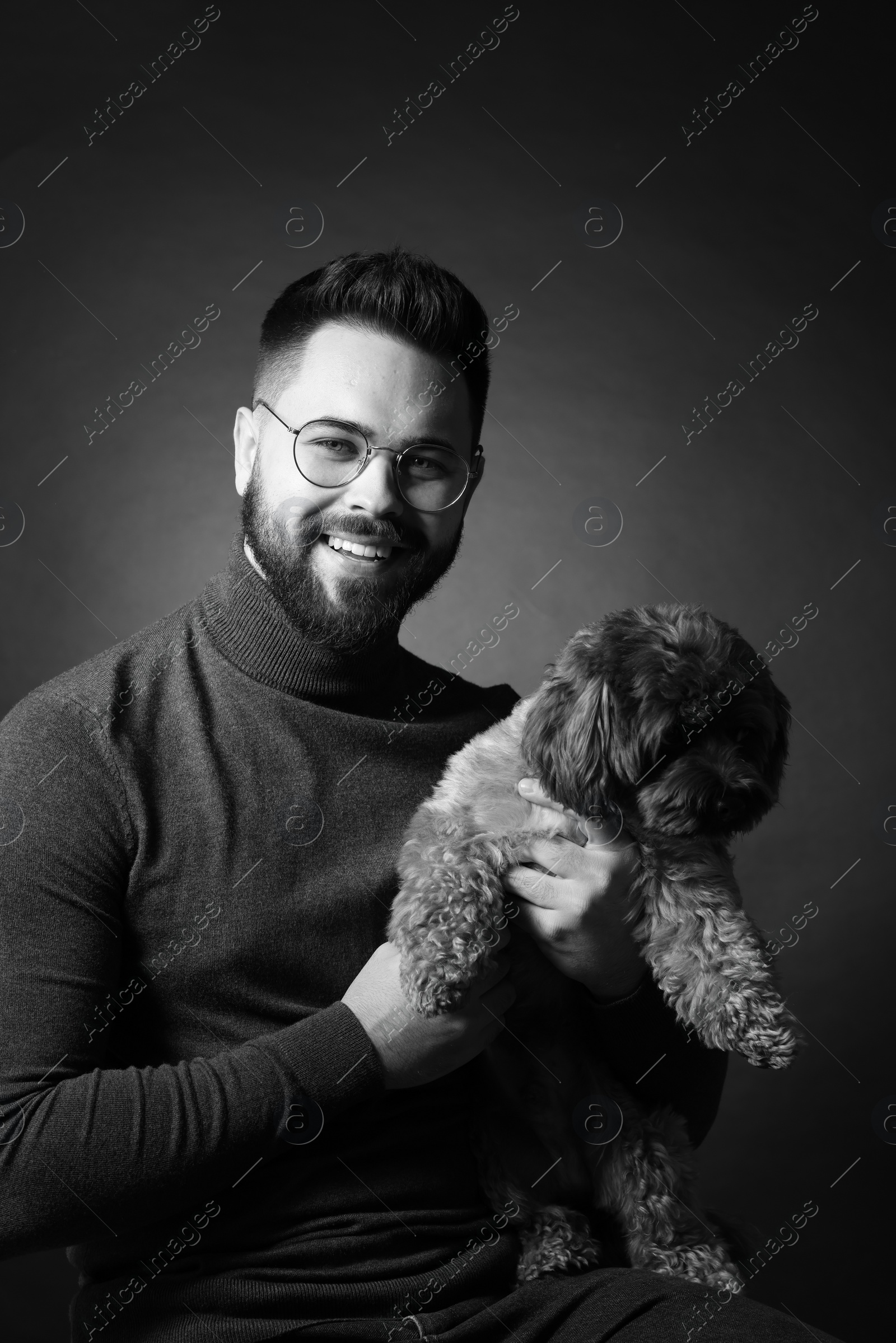 Photo of Handsome bearded man with cute dog on dark background. Black and white effect
