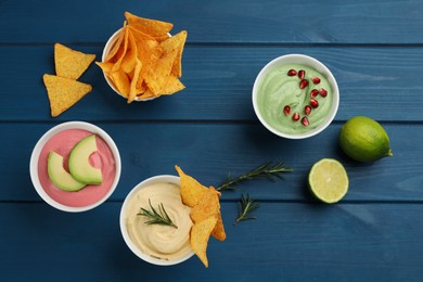 Photo of Different kinds of tasty hummus served with nachos on blue wooden table, flat lay