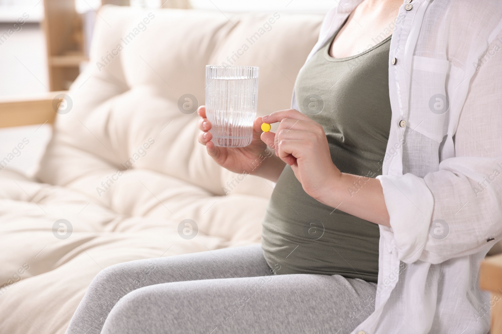 Photo of Pregnant woman holding pill and glass with water at home, closeup