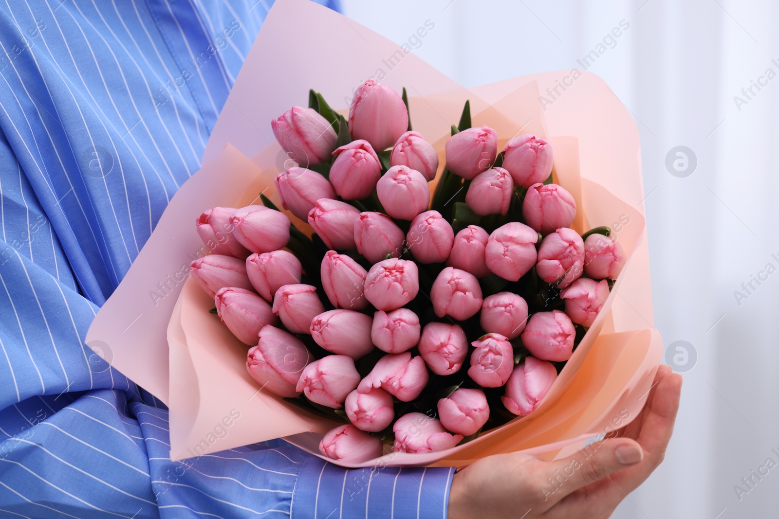 Photo of Woman holding bouquet of pink tulips indoors, closeup