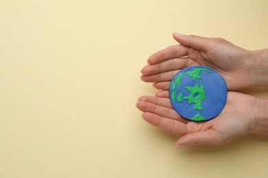 Photo of Woman holding model of planet on beige background, top view with space for text. Earth Day