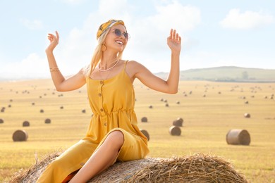 Beautiful hippie woman on hay bale in field, space for text