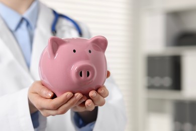 Photo of Doctor with pink piggy bank indoors, closeup. Space for text