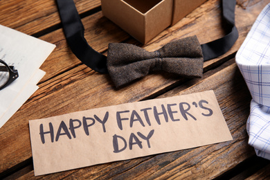 Photo of Paper with words HAPPY FATHER'S DAY and bow tie on wooden table