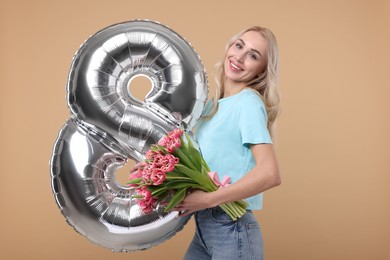 Photo of Happy Women's Day. Charming lady holding bouquet of beautiful flowers and balloon in shape of number 8 on beige background