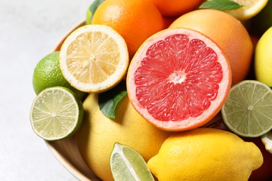 Photo of Different fresh citrus fruits and leaves in bowl on light table, closeup