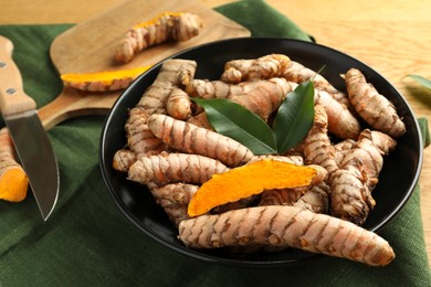 Photo of Bowl with raw turmeric roots and green leaves on table, closeup