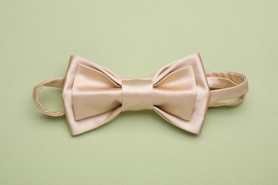 Photo of Stylish beige bow tie on pale green background, top view