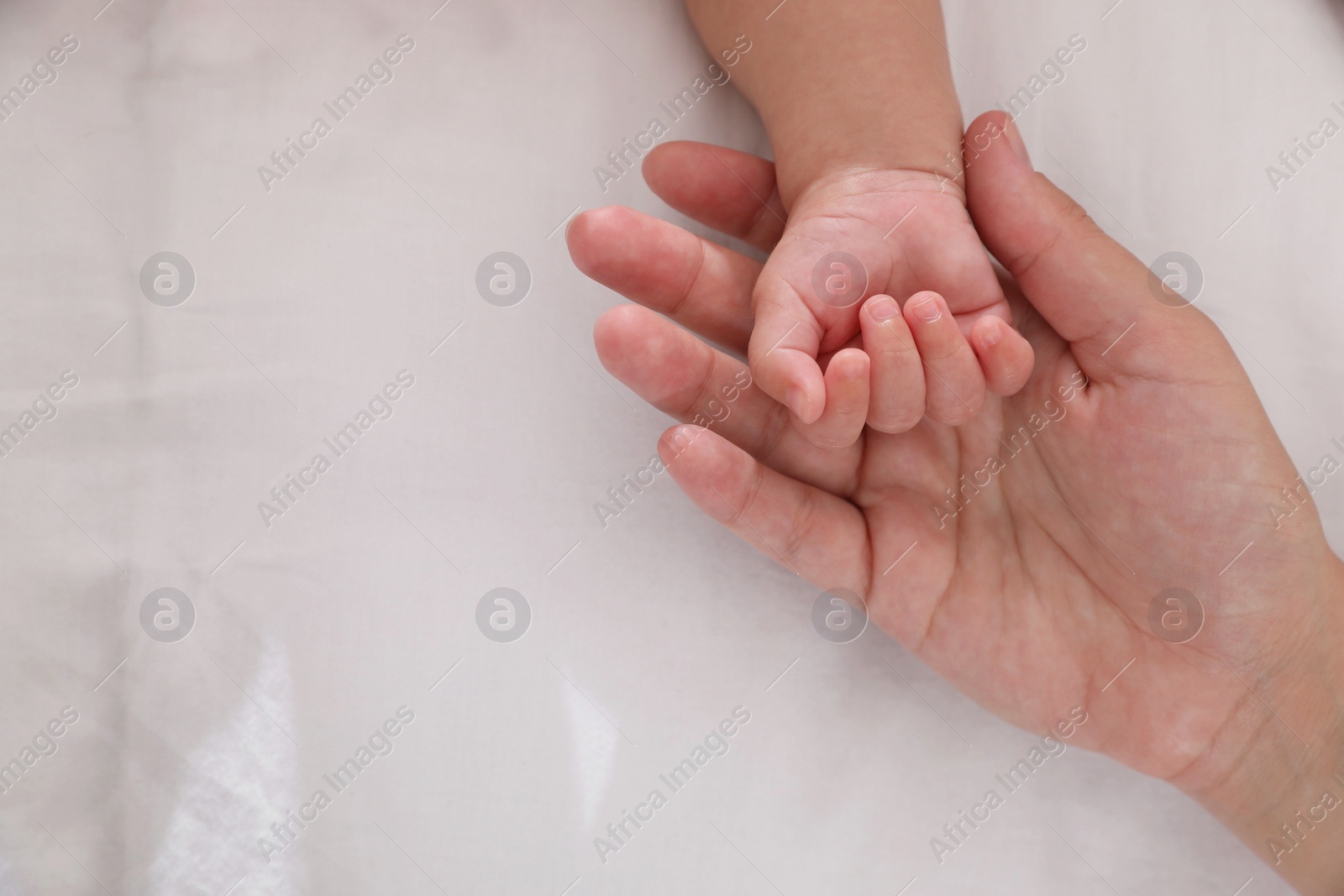 Photo of Mother with her baby on bed, closeup of hands. Space for text