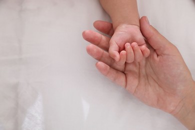 Mother with her baby on bed, closeup of hands. Space for text