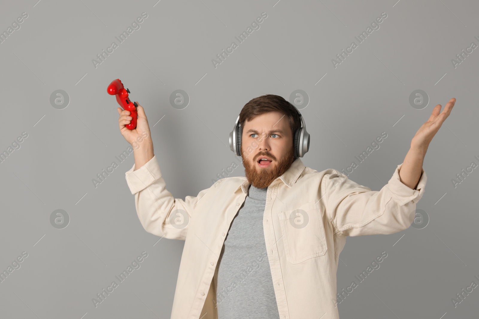 Photo of Confused man in headphones with game controller on grey background