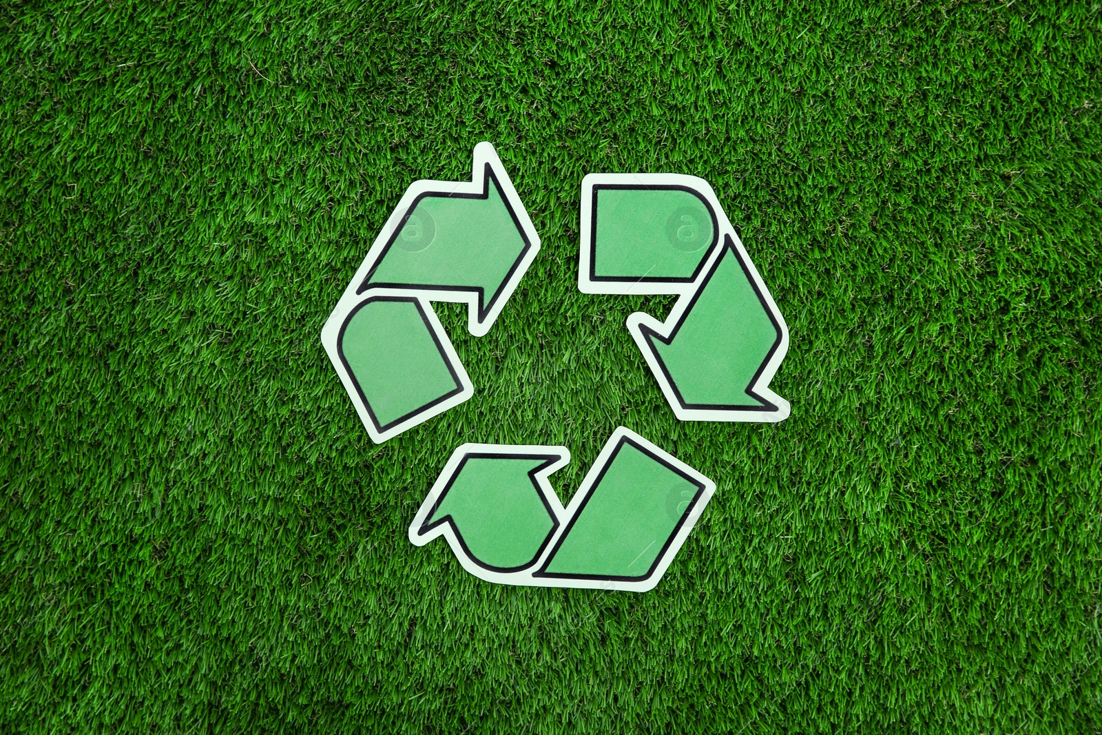 Photo of Paper recycling symbol on green grass, top view