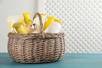Photo of Wicker basket full of different baby cosmetic products and toy on light blue wooden table. Space for text