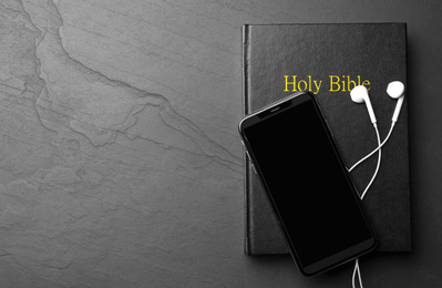 Photo of Bible, phone and earphones on black background, top view with space for text. Religious audiobook