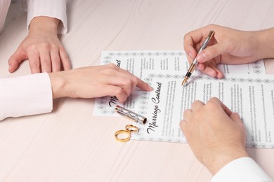 Man and woman signing marriage contract at light wooden table, closeup