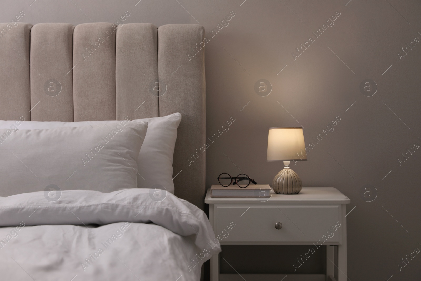 Photo of Stylish lamp, book and glasses on bedside table indoors. Bedroom interior elements