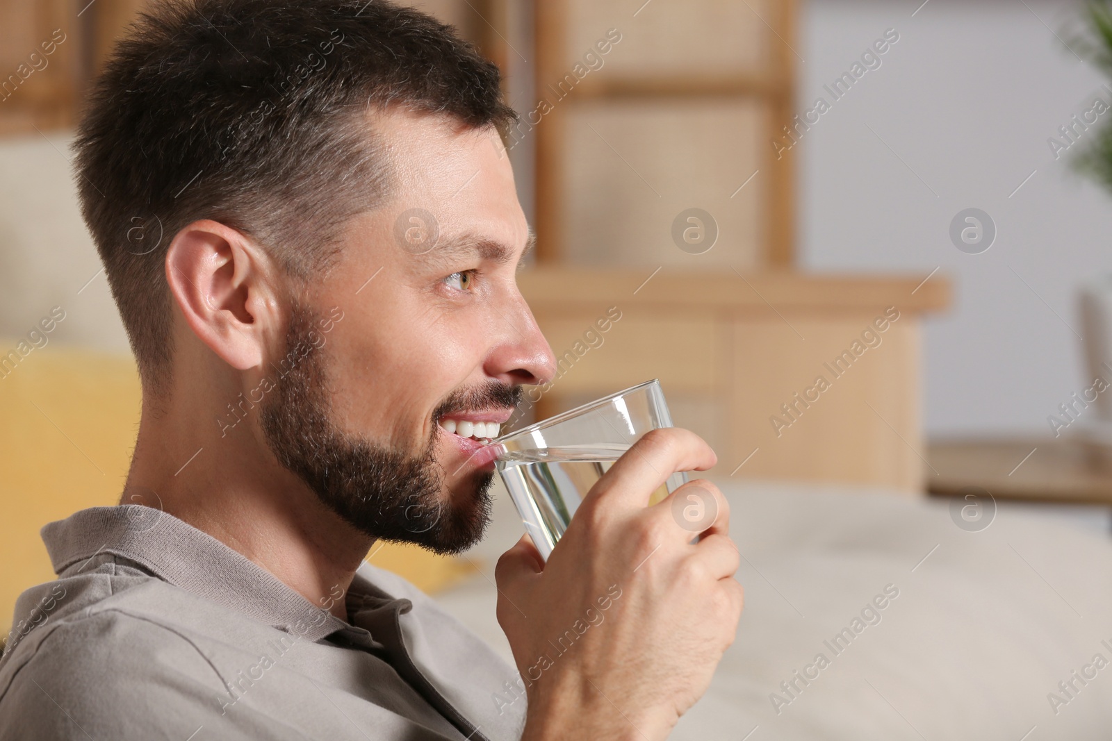 Photo of Happy man drinking water indoors. Refreshing drink