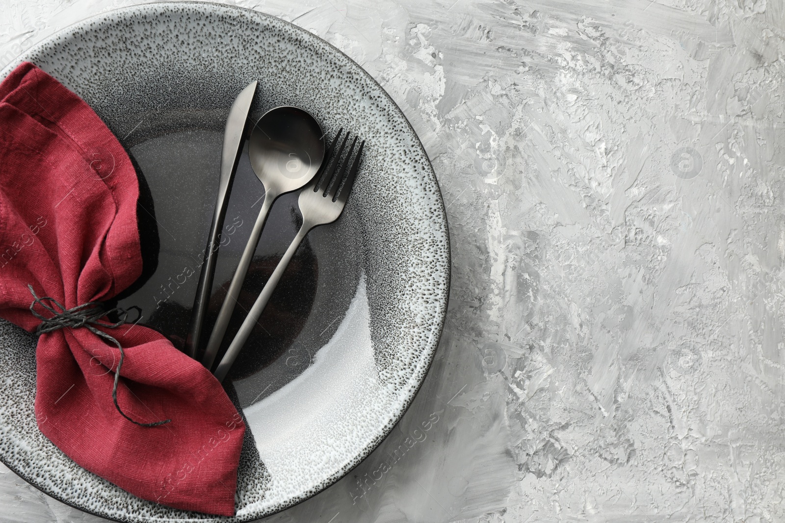 Photo of Stylish setting with cutlery, napkin and plate on grey textured table, top view. Space for text